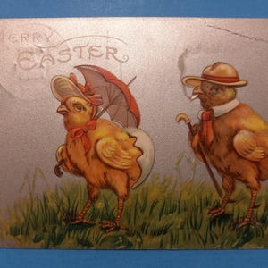 May include: A vintage postcard featuring a cartoon illustration of two chicks dressed in human clothing. One chick is wearing a hat and holding a cane, while the other chick is wearing a hat and holding an umbrella. The postcard has a silver background with the text "Merry Easter" in a circle at the top.