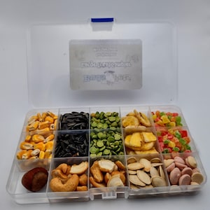 May include: A clear plastic container with 10 compartments filled with various bird seed and treats. The container has a blue latch and a label that reads "Bird Seed &  Treats".