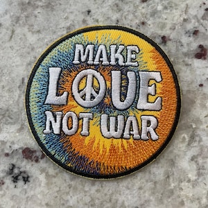 May include: A round, yellow, orange, and blue tie-dye patch with white embroidery that reads "Make Love Not War" and a peace sign.