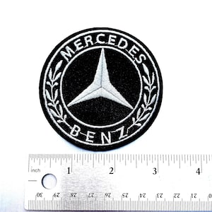 May include: A black and white embroidered patch featuring the Mercedes-Benz logo. The logo is a three-pointed star inside a circle with the words "Mercedes-Benz" around the outside. The patch is approximately 2 inches in diameter.