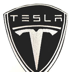 May include: Black and white embroidered patch with the word "TESLA" and a stylized "T" in the center.