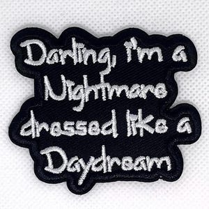 May include: Black embroidered patch with the phrase "Darling, I'm a Nightmare dressed like a Daydream" in white script. The patch has a wavy, irregular border. The text is in a cursive font.
