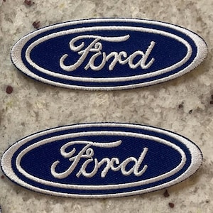 May include: Two embroidered patches featuring the Ford logo. The patches have a navy blue oval background with a white border and white script lettering. The Ford logo is a well-known automotive brand.