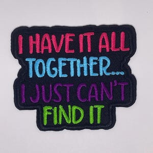 May include: A black embroidered patch with the text "I have it all together... I just can't find it" in pink, blue, purple, and green thread.