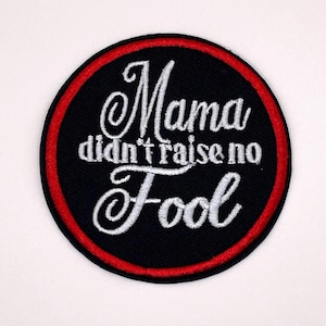 May include: Embroidered patch with the phrase "Mama didn't raise no Fool" in white script on a black background. The patch has a red border and is circular in shape.