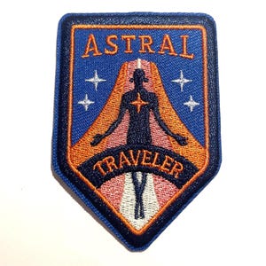 May include: Embroidered patch with the words "ASTRAL TRAVELER" in white and orange on a blue background. The patch features a silhouetted figure with outstretched arms, surrounded by orange and white accents, and four white stars.
