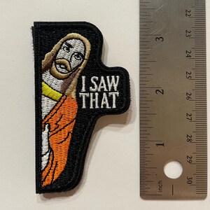 May include: A black and orange embroidered patch featuring a cartoon image of Jesus and the text "I SAW THAT".