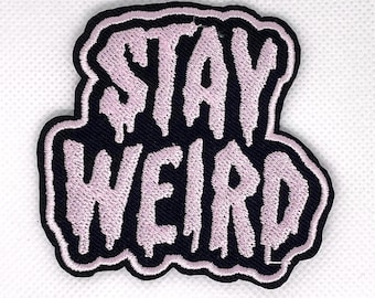 May include: Embroidered patch with the words "STAY WEIRD" in light pink, dripping font on a black background. The patch has a black border and is likely for clothing or accessories.