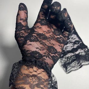 May include: A pair of black lace gloves with a ruffled cuff. The gloves are sheer and delicate, with a floral pattern.