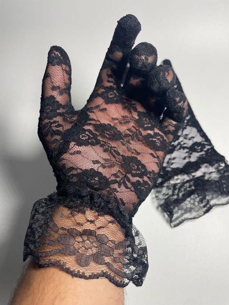May include: A pair of black lace gloves with a ruffled cuff. The gloves are sheer and delicate, with a floral pattern.