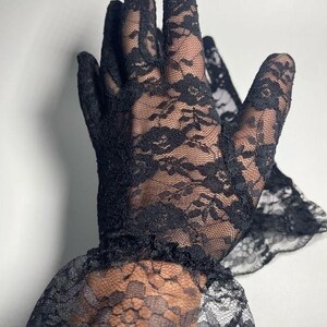 May include: A pair of black lace gloves with a ruffled cuff. The gloves are made of delicate, sheer lace with a floral pattern.