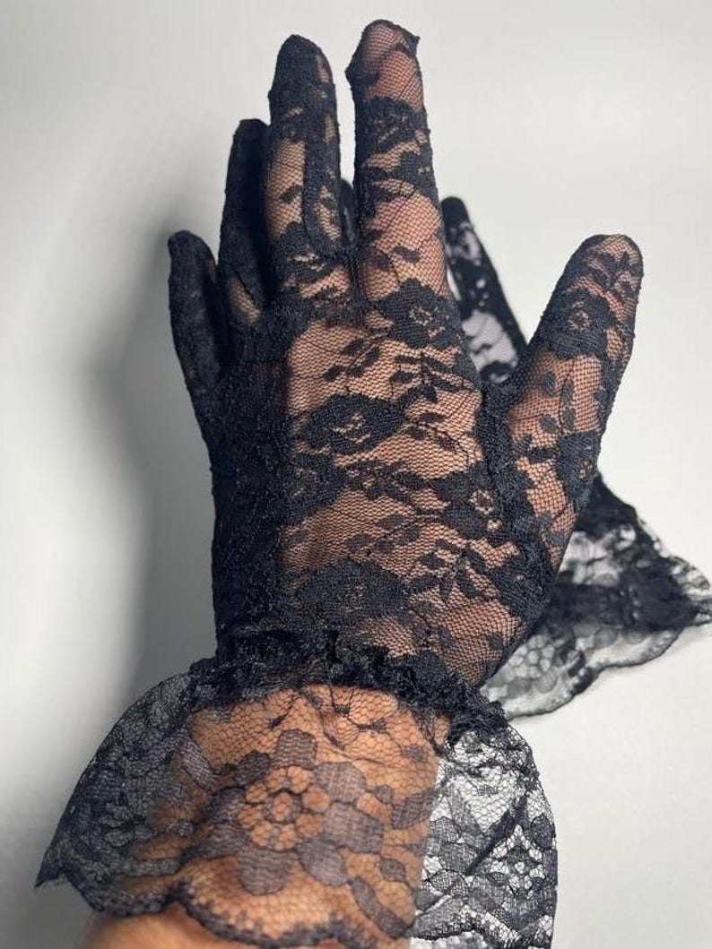 May include: A pair of black lace gloves with a ruffled cuff. The gloves are made of delicate, sheer lace with a floral pattern.