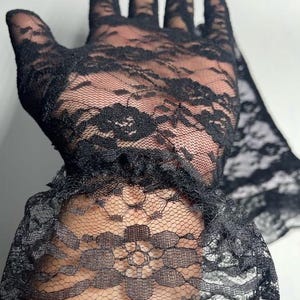 May include: Black lace gloves with a ruffled cuff. The gloves are made of delicate, sheer lace with a floral pattern.