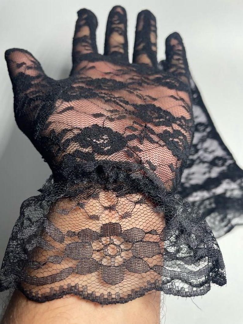 May include: Black lace gloves with a ruffled cuff. The gloves are made of delicate, sheer lace with a floral pattern.
