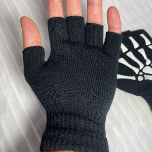 May include: Black fingerless gloves with a white skeleton design on the back of the hand.