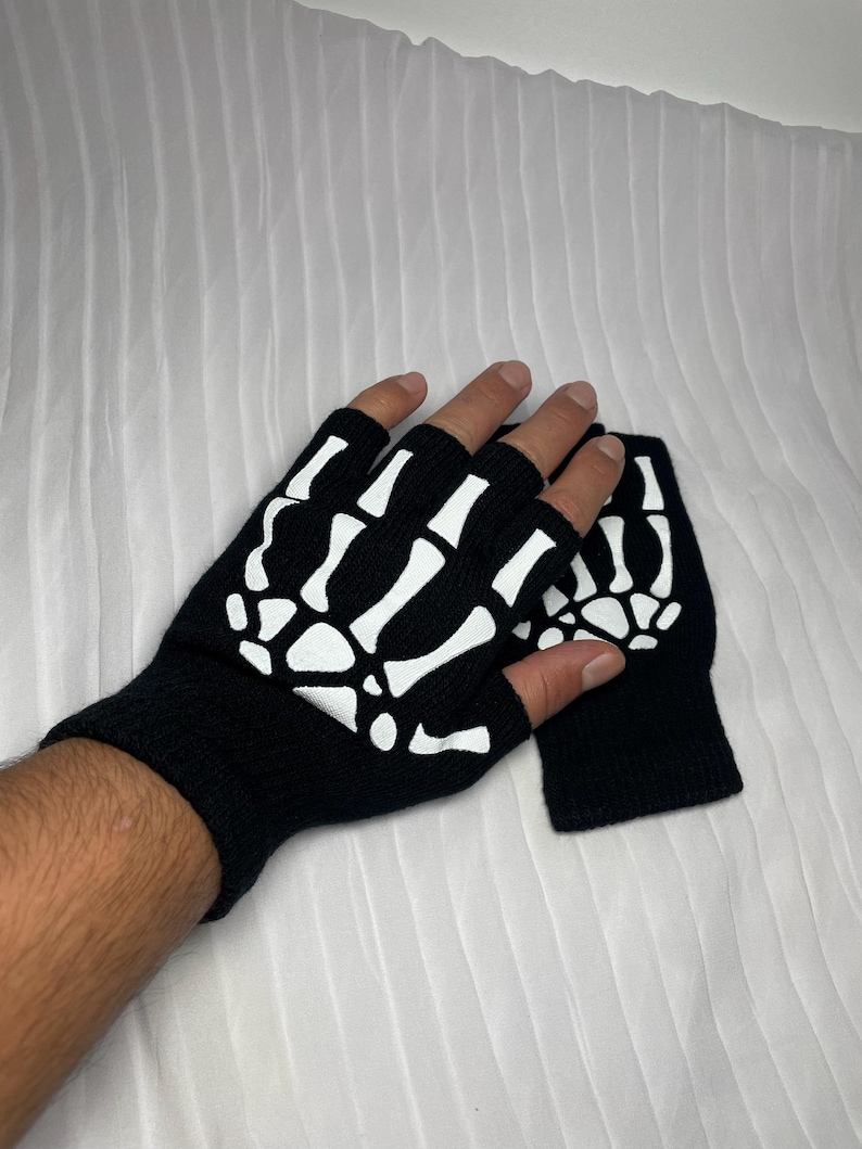 May include: A pair of black fingerless gloves with a white skeleton design. The gloves are made of a soft, knitted fabric.