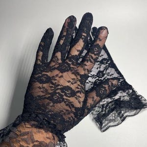 May include: A pair of black lace gloves with a ruffled cuff. The gloves are made of delicate lace with a floral pattern.
