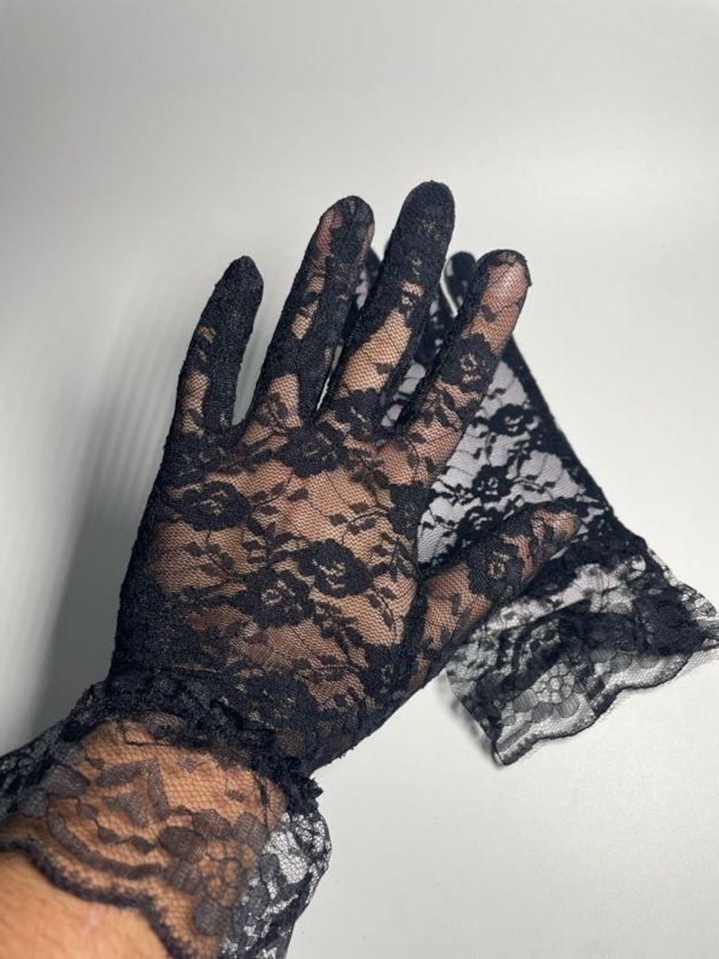 May include: A pair of black lace gloves with a ruffled cuff. The gloves are made of delicate lace with a floral pattern.