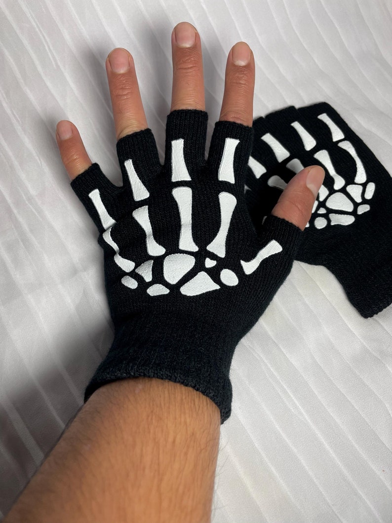 May include: A pair of black fingerless gloves with a white skeleton design. The gloves are made of a soft, stretchy fabric and are perfect for a spooky Halloween costume.