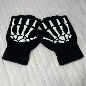 May include: A pair of black fingerless gloves with a white skeleton design. The gloves are made of a soft, knitted fabric.