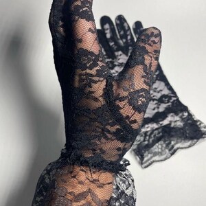 May include: A pair of black lace gloves with a ruffled edge. The gloves are made of delicate, sheer fabric with a floral pattern.
