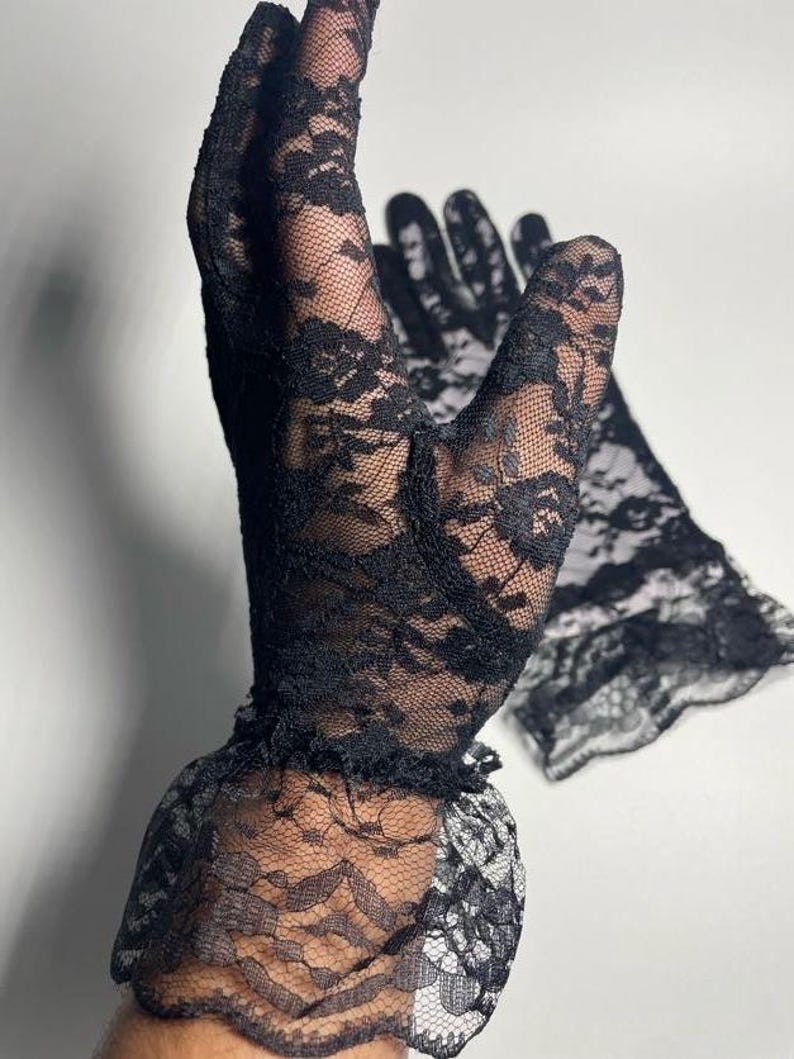 May include: A pair of black lace gloves with a ruffled edge. The gloves are made of delicate, sheer fabric with a floral pattern.