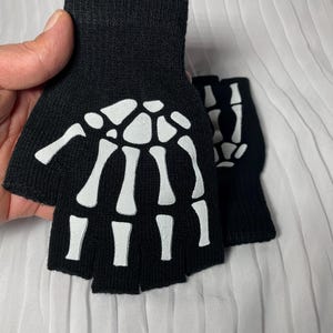 May include: A pair of black fingerless gloves with a white skeleton design.