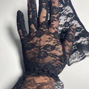 May include: A pair of black lace gloves with a ruffled cuff. The gloves are sheer and delicate, with a floral pattern.