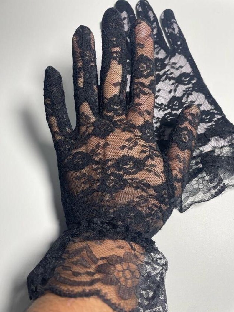 May include: A pair of black lace gloves with a ruffled cuff. The gloves are sheer and delicate, with a floral pattern.