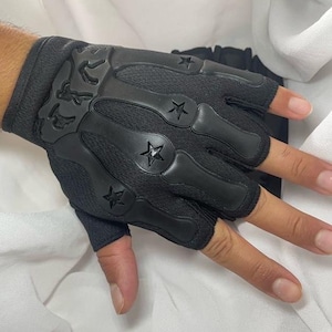 May include: Black fingerless gloves featuring star and skeleton bone patterns. The gloves are constructed from a blend of mesh and solid materials. They include a wrist cuff and are designed to leave the fingers exposed.