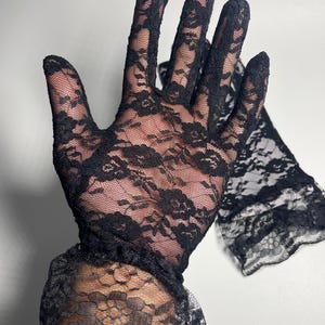 May include: A pair of black lace gloves with a ruffled cuff. The gloves are made of delicate, sheer lace with a floral pattern.