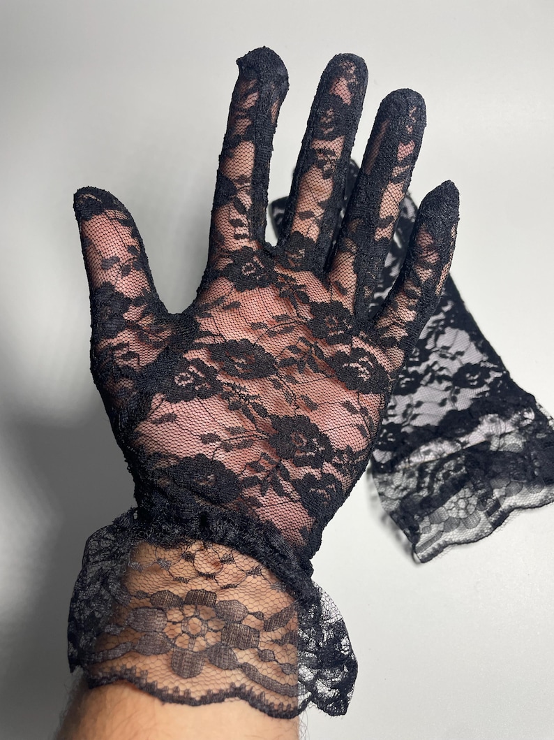May include: A pair of black lace gloves with a ruffled cuff. The gloves are made of delicate, sheer lace with a floral pattern.
