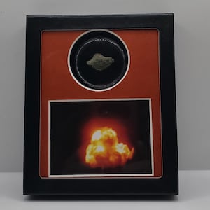 Op de afbeelding: Zwart omkaderde presentatie met een rode achtergrond. Het bevat een klein, onregelmatig gevormd, groenbruin object in een cirkel en een afbeelding van een oranje en gele explosie.