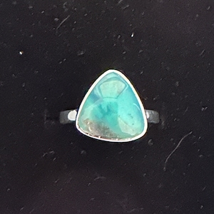 May include: A silver ring with a triangular green gemstone. The gemstone has a light green color with darker green inclusions.