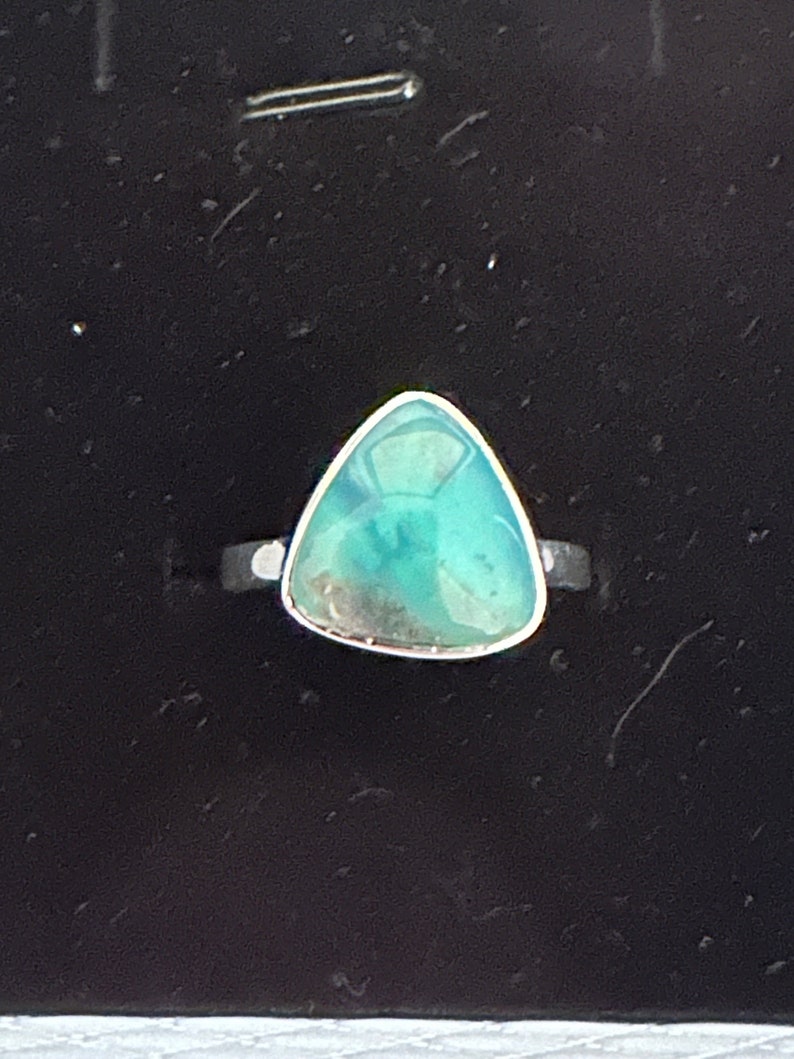 May include: A silver ring with a triangular green gemstone. The gemstone has a light green color with darker green inclusions.