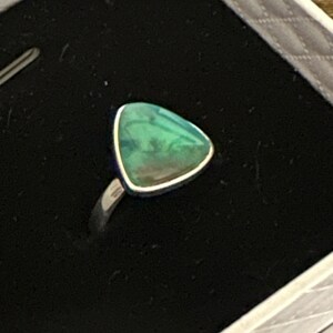 May include: A silver ring with a triangular green gemstone.