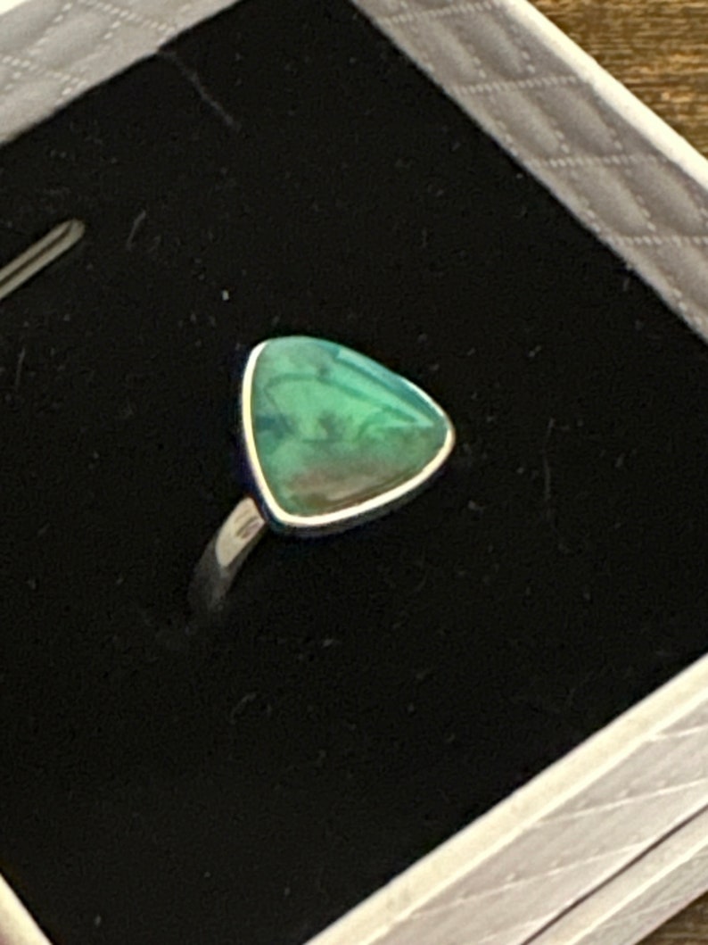 May include: A silver ring with a triangular green gemstone.