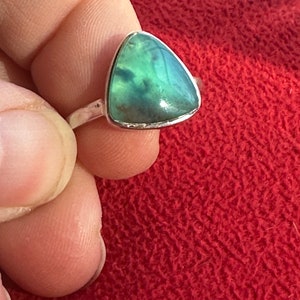 May include: A silver ring with a triangular green gemstone. The gemstone has a cloudy, marbled pattern.
