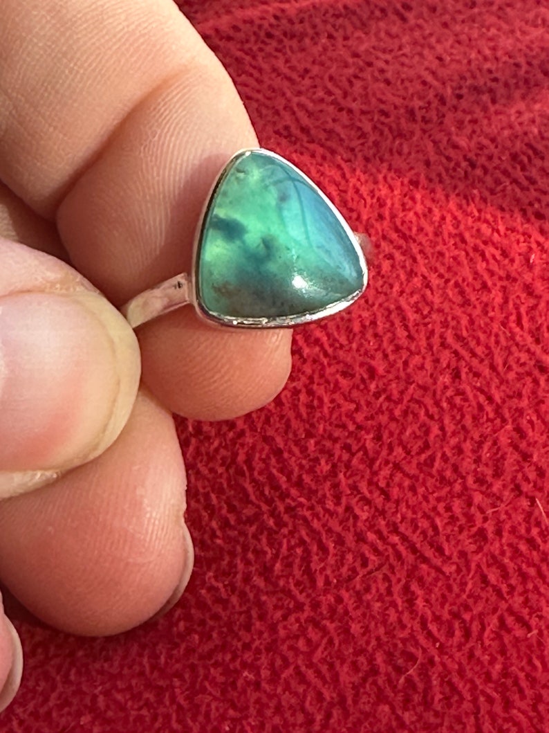 May include: A silver ring with a triangular green gemstone. The gemstone has a cloudy, marbled pattern.