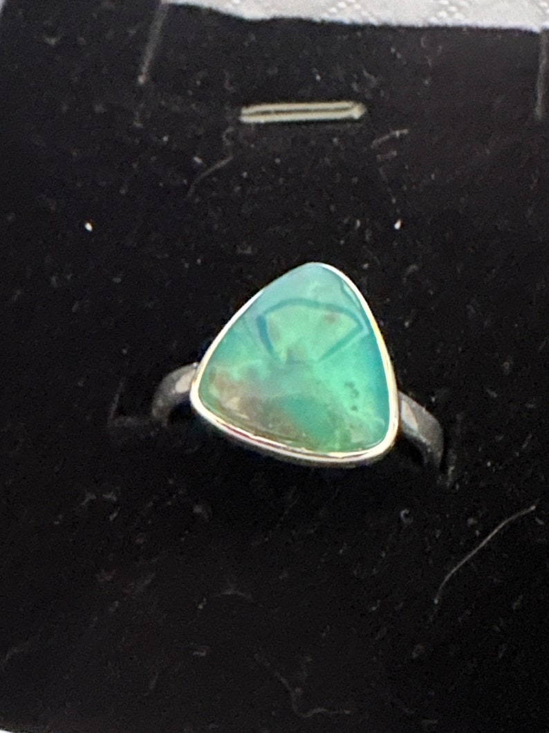 May include: A silver ring with a triangular green gemstone.