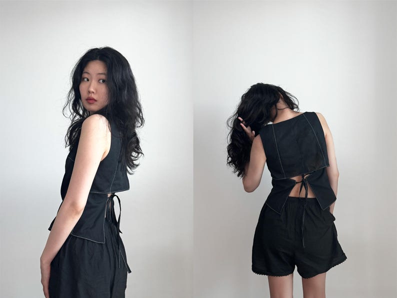 May include: A black sleeveless top featuring a square neckline, white contrast stitching along the edges, and a tie-back closure at the waist, paired with black shorts that have a scalloped hemline detail along the bottom edge of the fabric.
