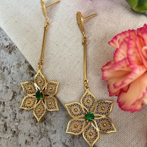 May include: Gold dangle earrings with a green gemstone in the center of a filigree flower design.