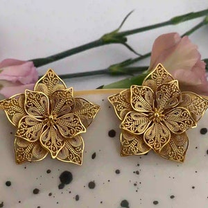 May include: A pair of gold filigree flower earrings. The earrings are made of delicate, intricate metalwork and have a floral design.