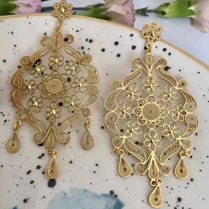 May include: A pair of gold filigree earrings with a floral design. The earrings are intricate and delicate, with a dangling drop design.