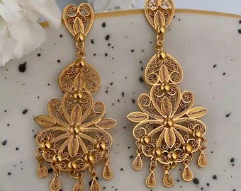 May include: A pair of gold filigree earrings with a heart-shaped top and a flower-shaped bottom. The earrings have a dangling design with small beads and teardrop-shaped accents.