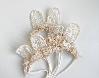 May include: A set of three white lace bunny ear headbands with delicate floral embellishments. The headbands are made of soft elastic and are perfect for adding a touch of whimsy to any outfit.
