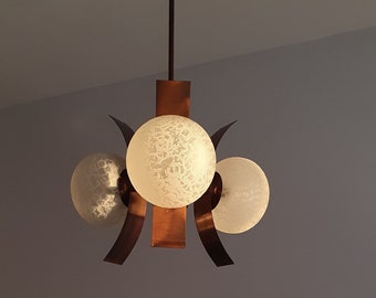 May include: A vintage ceiling light fixture with three frosted glass globes and copper-colored metal accents. The fixture is suspended from a dark brown rod and mounted to the ceiling. The light is casting a warm glow.