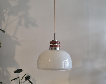 May include: A white glass pendant light with a chrome and wood trim. The light is hanging from a cord.
