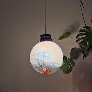 May include: A white glass globe pendant light with a black metal fixture and a clear light bulb. The globe has a swirling pattern of white and blue, with a hint of orange at the bottom.