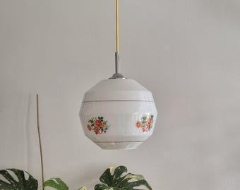 May include: A white, floral patterned, globe-shaped pendant light fixture with a yellow cord hanging from a white ceiling.